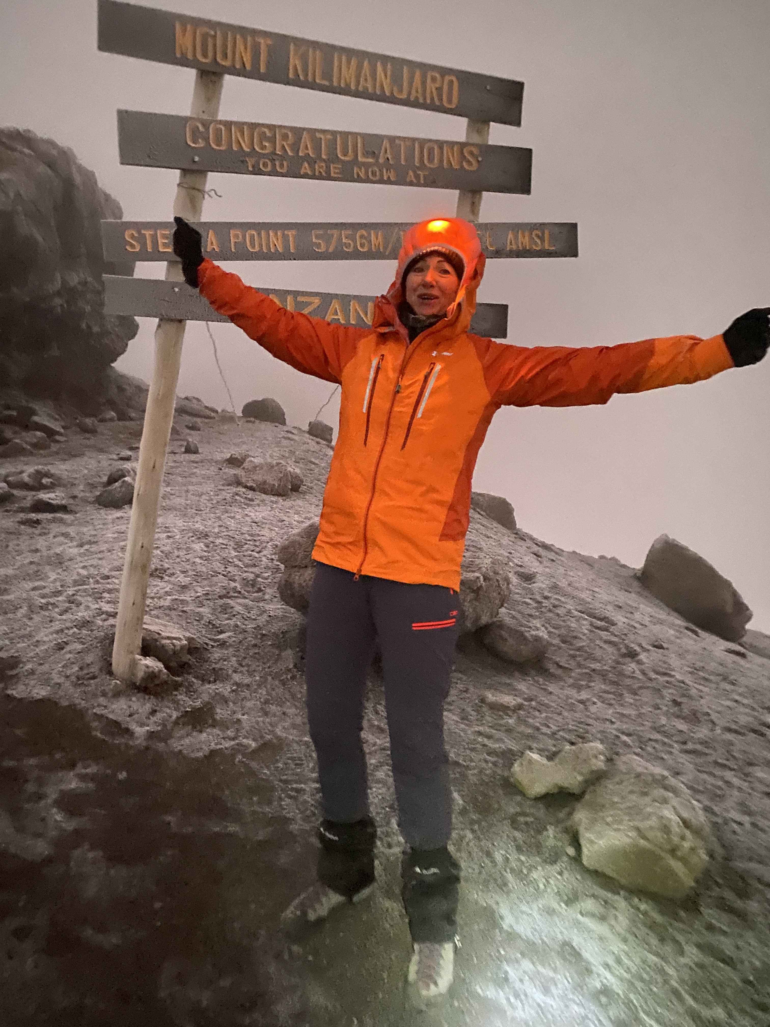 A climber with arms outstretched at the Stella Point summit sign on Kilimanjaro at dawn