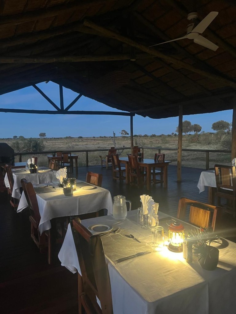 Tables set for dinner on the thatched restaurant deck at Mababe River Lodge at dusk, looking over the floodplain