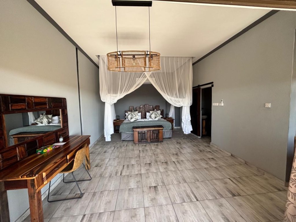 A bright lodge room at Mababe River Lodge with a netted double bed, writing desk and tiled floor