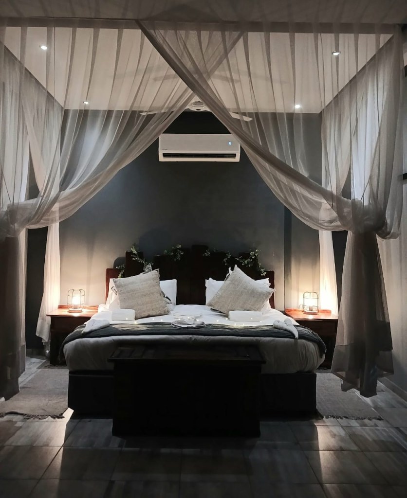 A lodge room at Mababe River Lodge at night, with a four-poster net bed and lantern lighting