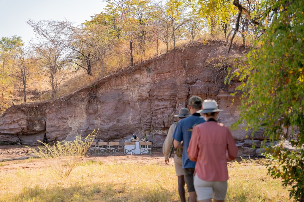 Ranger and guests on a walking safari beneath the Matusadona escarpment, with a riverbed brunch table set out