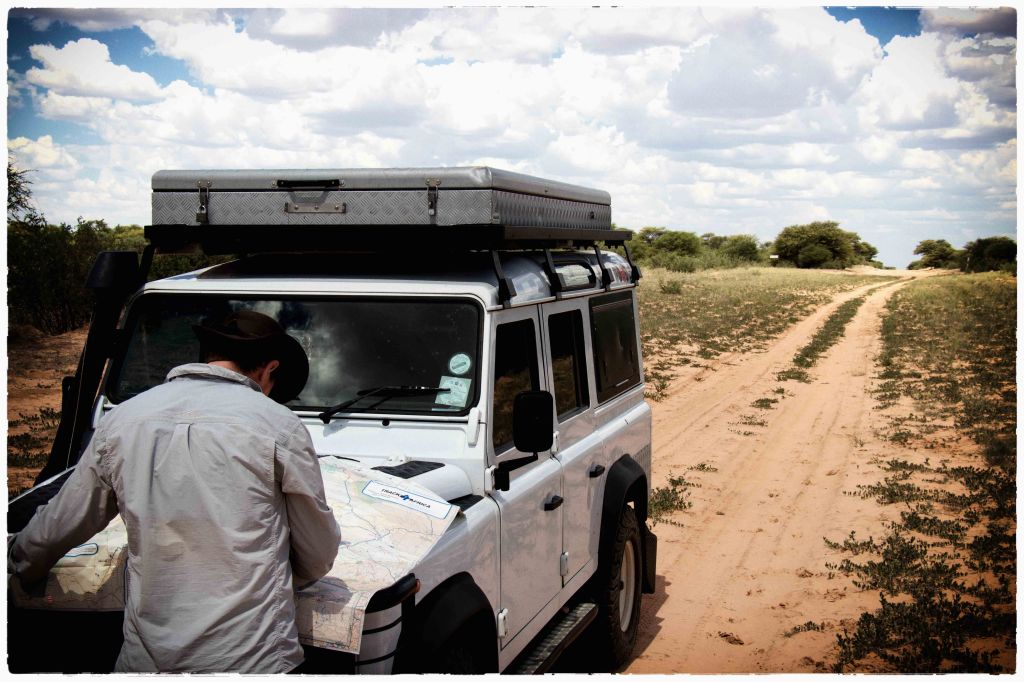 Johann Groenewald consulting a paper map beside a Land Rover in the Kalahari